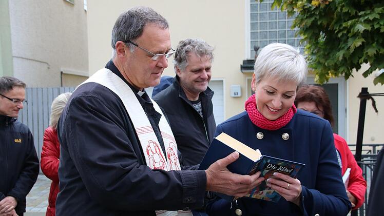 Pfarrer Georg Birkel (links) ließ alle bei der Einweihung Anwesenden eine Bibel signieren, die er dann in den Schrank stellte. Monika Stich (rechts) und ihr Team von der Frauen-Union betreuen den Schrank.