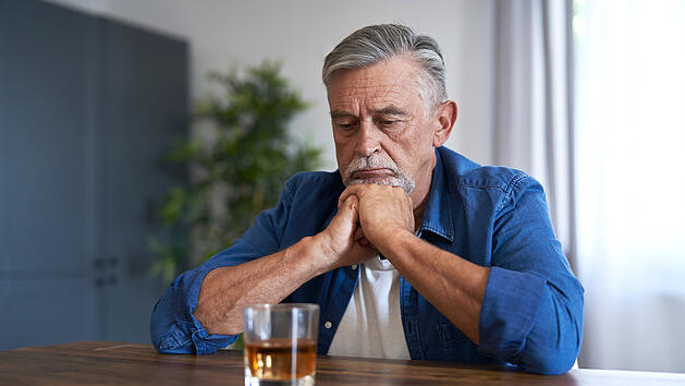 Älterer Mann sitzt vor einem Glas Whiskey