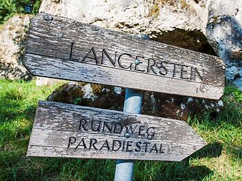 Ein verwittertes Holzschild zeigt den Weg zu "Langerstein" und "Rundweg Paradiestal", vor einem Felsen im Gr&uuml;nen in der Fr&auml;nkischen Schweiz.