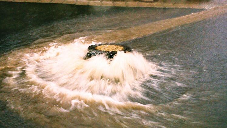 Als wir in unserem Heimatort Kirchlauter ankamen, nachdem wir in Ebelsbach ein bis zwei Zentimeter große Hagelkörner erdulden mussten, offenbarte sich uns ein Bild des Schreckens: An der Kreuzung die den Schneckenhügel von der alten Siedlung und der Hauptstraße trennt, riss es den Gulli aus der Verankerung. Das Wasser aus dem Schneckenhügel und der alten Siedlung fließt durch diesen Kanal und der Gully konnte dem Druck (wieder einmal) nicht standhalten. Sofort zückten wir das Handy und liefen...