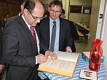 Christian Schmidt, Bundesminister für Landwirtschaft und Ernährung (links, oberes Foto), trägt sich unter den Augen von Bürgermeister Wolfram Thein in das Goldene Buch der Marktgemeinde Maroldsweisach ein.