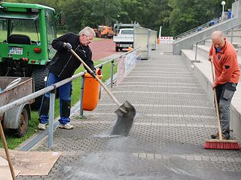Bei einem Arbeitseinsatz kehren Gerd Zeitler (links) und Günter Scheuring Split in das Steinpflaster auf dem Gehweg am Spielfeldrand ein. Der TSV richtet im Zuge der Hallensanierung unter anderem die Tribüne her.