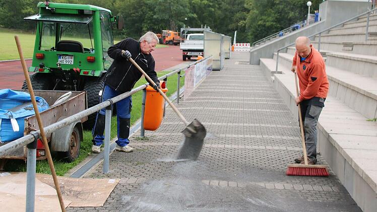 Bei einem Arbeitseinsatz kehren Gerd Zeitler (links) und Günter Scheuring Split in das Steinpflaster auf dem Gehweg am Spielfeldrand ein. Der TSV richtet im Zuge der Hallensanierung unter anderem die Tribüne her.