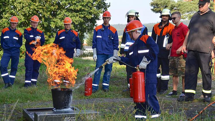 Feuerprobe in Lauter: Paul Pfrang löscht hier seinen ersten Fettbrand am Brandsimulator. Nicht nur seine Stralsbacher Kameraden schauen zu, auch die Lauterer Organisatoren, darunter Daniel Lang (rechts), der die 24-Stunden-Übung angeregt hatte. Foto: Kathrin Kupka-Hahn