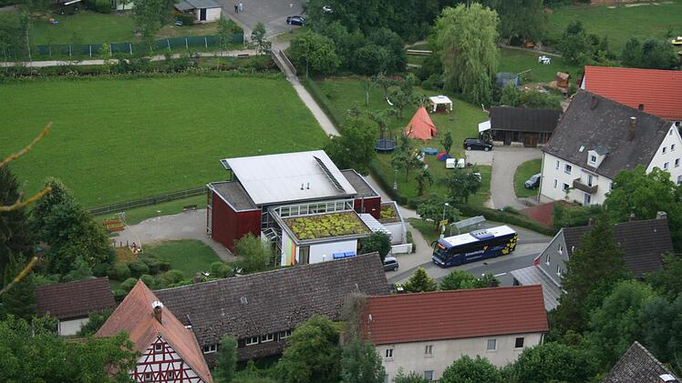 Der Kindergarten Egloffstein im jetzigen Zustand. Das rote Gebäude ist die Kita, davor ein kleiner Anbau mit begrüntem Flachdach. Links vom Anbau soll auf Anregungen des Architekten der zweigeschossige Neubau hin.  Kritiker wollen diesen weiter nach unten schieben und an den roten Bau anschließen lassen, damit oben ein Spielplatz entstehen kann. Foto: Reinhard Löwisch