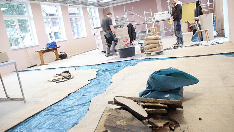Zwei Bodenleger gießen die Lücken zwischen dem Asphaltestrich mit Epoxitestrich aus. Dort, wo vorher Wände im Hainer Kulturhaus standen oder der Asphalt weggebröckelt war, wurde blaue Folie auf den Beton gelegt, damit der neue Estrich nicht festklebt. Wenn diese Reparatur beendet ist, wird der Boden noch mit Gewebe gespachtelt. Dann kommt der Belag drauf. Die Hainer Bürger bringen am Samstag die Platten in der abgehängten Decke an.  Foto: Friedwald Schedel