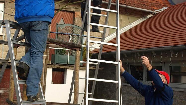 Hubert Schott, Manfred Wolf und Herbert Häuslein (von links) hängen an einem Baum  vor dem Dorfplatz Christbaumbeleuchtung auf.