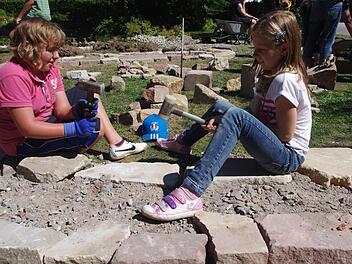 Linda Kopp und Sofia Fischer (von links) schlagen mit einem Hammer auf große Steine, damit das Fundament des Kräuter-Rondells eben wird.  Foto: Heike Schülein