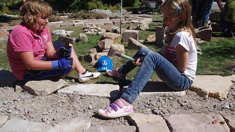 Linda Kopp und Sofia Fischer (von links) schlagen mit einem Hammer auf große Steine, damit das Fundament des Kräuter-Rondells eben wird.  Foto: Heike Schülein