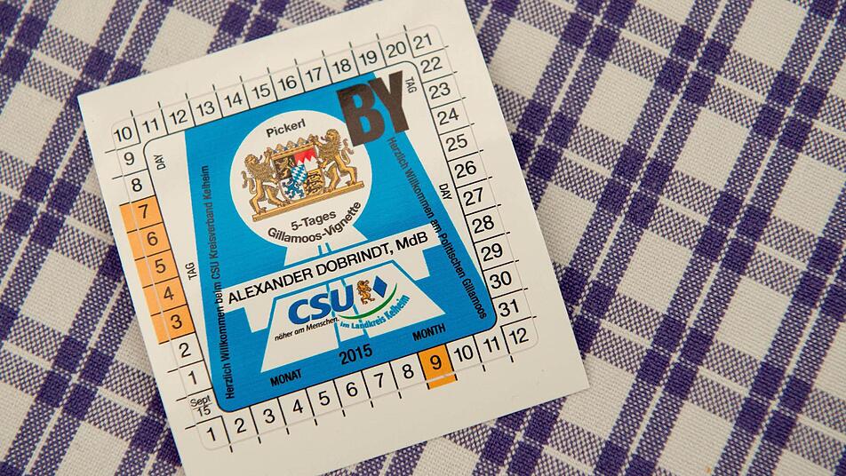 Eine fiktive Maut-Plakette mit der Aufschrift "Alexander Dobrindt - 5-Tages Gillamoos-Vignette" liegt am 08.09.2014 in Abensberg (Bayern) beim politischen Gillamoos-Frühschoppen auf einem Tisch. Das Gillamoos ist eines der größten und ältesten Volksfeste Niederbayerns und bietet traditionell einen politische Schlagabtausch der Parteien. Foto: Sven Hoppe/dpa