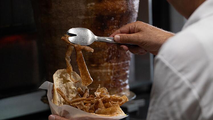 Ein Mensch f&uuml;llt einen D&ouml;ner mit frisch geschnittenem Fleisch. Im Hintergrund ist ein D&ouml;ner-Spie&szlig; zu sehen.