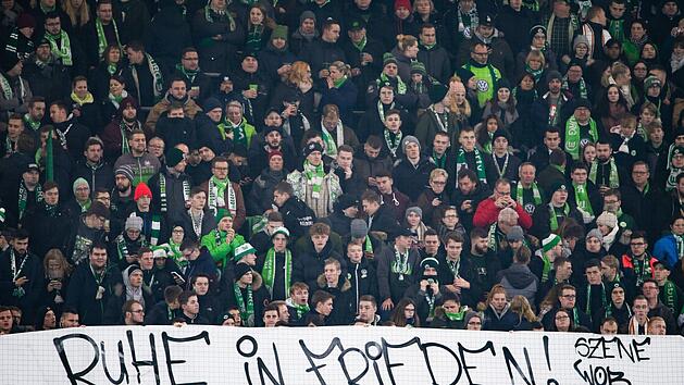 Fans vom VfL Wolfsburg halten ein Plakat mit der Aufschrift "Ruhe in Frieden!". Auf dem Weg zum Fu&szlig;ballspiel sein ein Fan des FC Schalke 04 in der N&auml;he des Stadions zusammengebrochen und verstarb sp&auml;ter, sagte ein Polizeisprecher. Foto: Swen Pf&ouml;rtner/dpa