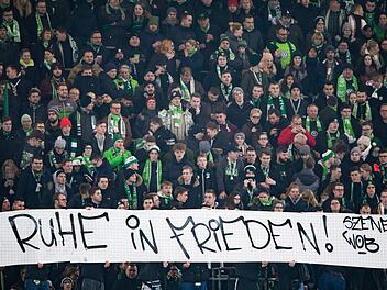 Fans vom VfL Wolfsburg halten ein Plakat mit der Aufschrift "Ruhe in Frieden!". Auf dem Weg zum Fu&szlig;ballspiel sein ein Fan des FC Schalke 04 in der N&auml;he des Stadions zusammengebrochen und verstarb sp&auml;ter, sagte ein Polizeisprecher. Foto: Swen Pf&ouml;rtner/dpa