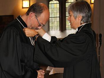 Regionalbischöfin Dorothea Greiner legte dem neuen Dekan Thomas Kretschmar, der zuletzt in Kaufbeuren tätig war, die Hand auf und hängte ihm das Kreuz um: Damit installierte sie ihn offiziell in seinem neuen Amt.  Foto: Sonny Adam