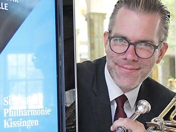 Posaunist Roman Riedel an einer Werbesäule, die auf den neuen Namen des Kurorchesters hinweist.  Foto: Borst
