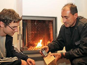 Bezirkskaminkehrermeister Hilmar Stadter (rechts) nimmt   im Haus von Christian Wagner (links) und Carina Kanis  den  Speicherofen unter die Lupe. Er  misst dabei auch   die Feuchtigkeit des Holzes. Foto Alexander  Hartmann