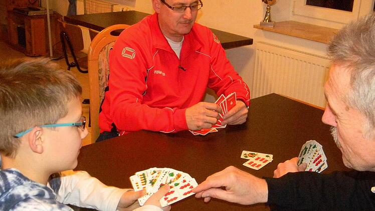Fritz Trautner (r.) bringt Bastian das Schafkopfen bei. Bastian Vater Andreas Schnell (M.) begrüßt das Interesse seines Sohns.  Foto: Lengenfelder