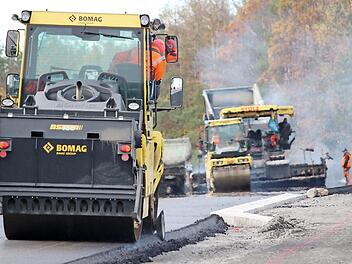 Der heiße Asphalt (hinten) dampft noch, während eine Maschine (im Vordergrund) bereits die Kanten glättet. Nach zwei Tagen sind die Asphaltierungsarbeiten an der Strecke zwischen Ibind und er B303 weit fortgeschritten. Foto: Eckehard Kiesewetter