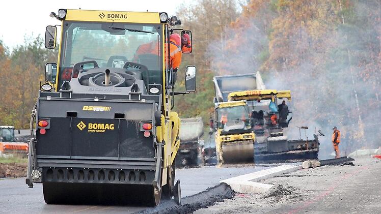 Der heiße Asphalt (hinten) dampft noch, während eine Maschine (im Vordergrund) bereits die Kanten glättet. Nach zwei Tagen sind die Asphaltierungsarbeiten an der Strecke zwischen Ibind und er B303 weit fortgeschritten. Foto: Eckehard Kiesewetter