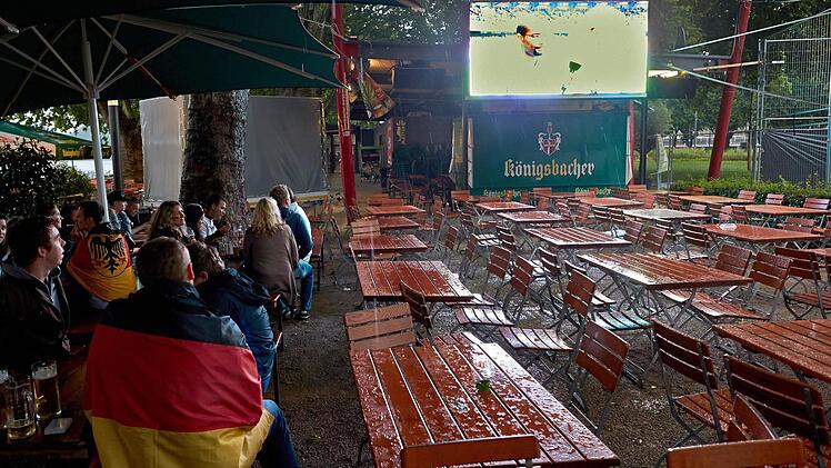 Public Viewing im Jahr 2022? Fußballfans sitzen in einem Biergarten, Der Sonnenschirm dient allein dem Regenschutz. Foto: Thomas Frey/dpa