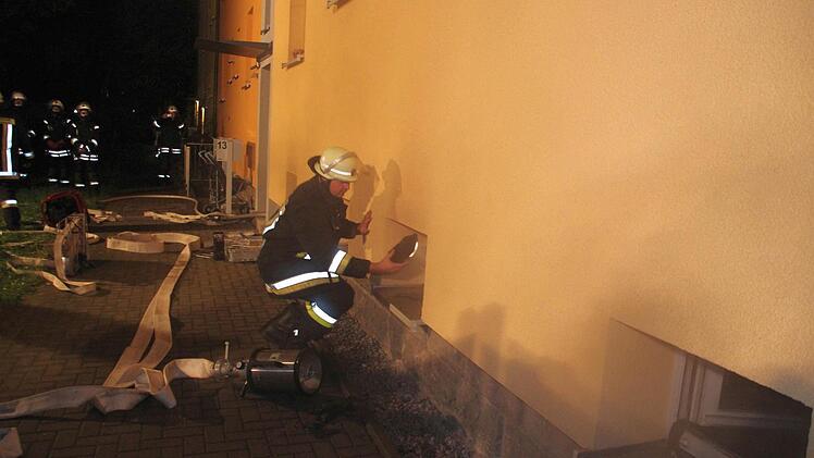 Ein Feuerwehrmann leuchtet durch die kaputte Scheibe des Kellerfensters.  Foto: Friedwald Schedel