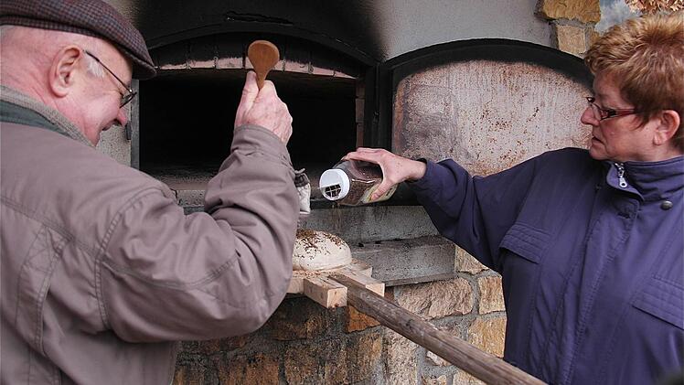 Bevor die Brote im Ofen landen, sticht Werner Kühnreich mit einem Holzstäbchen Löcher in die Oberfläche des Teiges und Anita Henning streut Kümmel drauf.