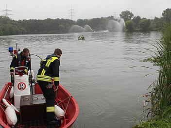 Männer der Feuerwehr Lichtenfels/Main - Gefahrenschutzzug - starten ihr Boot, während Kollegen schon auf dem See fahren, um Bewegung ins Wasser zu bringen und damit die Sauerstoffzufuhr zu erhöhen. Am anderen Ufer pumpen Feuerwehrleute sauerstoffreiches Mainwasser in Fontänen in den See. Foto: Popp