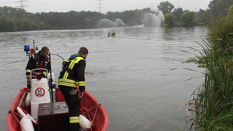 Männer der Feuerwehr Lichtenfels/Main - Gefahrenschutzzug - starten ihr Boot, während Kollegen schon auf dem See fahren, um Bewegung ins Wasser zu bringen und damit die Sauerstoffzufuhr zu erhöhen. Am anderen Ufer pumpen Feuerwehrleute sauerstoffreiches Mainwasser in Fontänen in den See. Foto: Popp