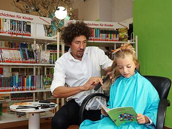 Danny Beuerbach schneidet Julia zwischen Bücherregalen die Haarspitzen.Foto: Arkadius Guzy