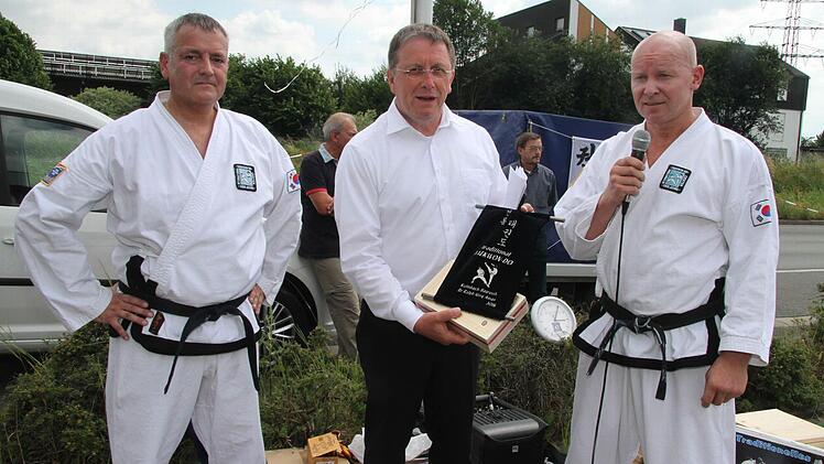Schwarzgurt-Inhaber Rainer Weber und Ralph Aman (6. Dan, rechts) überreichten OB Schramm einen Erinnerungs-Wimpel.