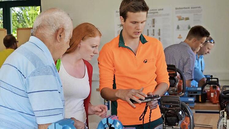 Tim Hartung ist Auszubildender im zweiten Lehrjahr. Hier erklärt der angehende Forstwirt Wissenswertes zur Motorsäge. Interessiert verfolgen die Besucher Anna Viktoria Kaiser und Hans Hartmann seine Ausführungen. Fotos: Kathrin Kupka-Hahn