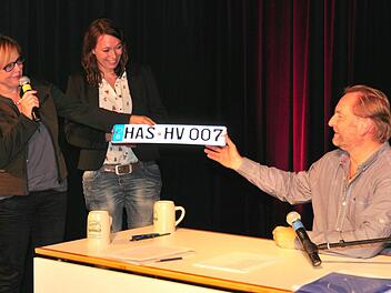 Das hat Helmut Vorndran nun davon, dass er so gerne über die Autofahrer mit HAS-Kennzeichen schimpft: Petra Lettang vom Kulturamt Haßfurt (links) und Stefanie Schleicher von der Buchhandlung Hübscher nahmen den Autor in den "Club der famosesten Autofahrer" auf und überreichten ihm ein neues Nummernschild: "HAS HV 007" sowie einen Gutschein für eine Fahrstunde bei einer Haßfurter Fahrschule. Foto: Ulrike Langer
