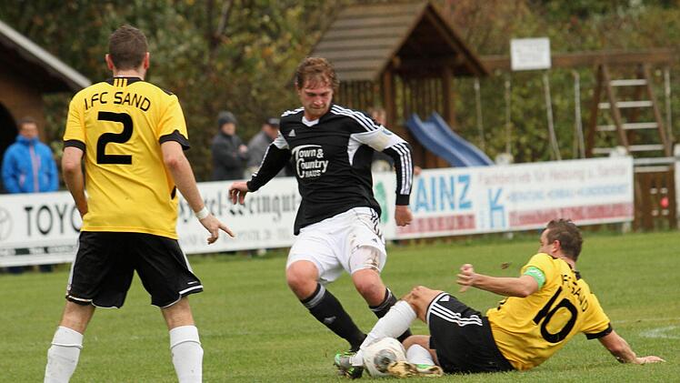 Ein großes Laufpensum absolvierte wieder der Sander Kapitän Daniel Rinbergas (rechts), der in der Abwehr aushilft und mit einer Grätsche den Augsfelder Mittelstürmer Peter Hertel stoppt. Links Andre Schmitt.