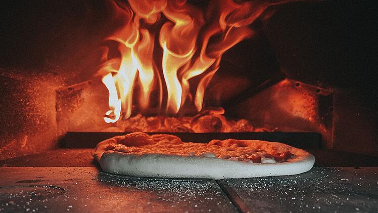 Ein Holzofen mit lodernden Flammen, darin eine Pizza, die bäckt. Ein Symbol für die Pizzeria "Trieste", die sich emotional verabschiedet.
