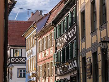 Eine charmante Straße mit bunten Fachwerkhäusern und verzierten Fensterläden, typisch für malerische fränkische Städte. Die Fachwerkarchitektur ist detailreich und historisch.