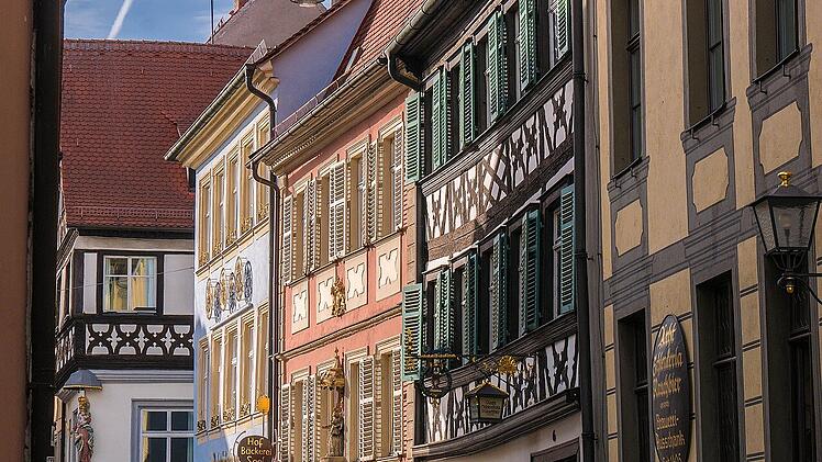 Eine charmante Straße mit bunten Fachwerkhäusern und verzierten Fensterläden, typisch für malerische fränkische Städte. Die Fachwerkarchitektur ist detailreich und historisch.