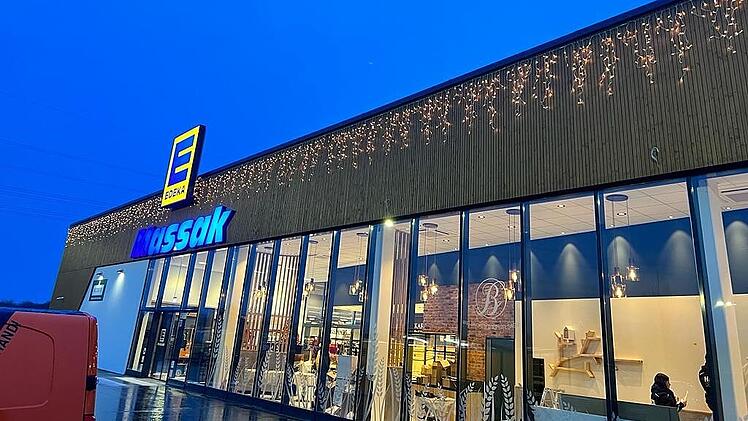 Der neue Edeka-Markt in Hallstadt zeigt eine moderne Fassade mit gläserner Front und Weihnachtsbeleuchtung. Eine Bäckerei mit Café ist ebenfalls integriert.
