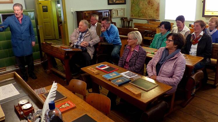 Museumsleiter Günter Wild (links) in seinem Element. Seine Schüler (von links) Helmut Moncken, Werner Reimann und Herbert Schmidt sowie (rechts, von vorne nach hinten) Rita Huber, geb. Weigel, Gertraud Wölfel, geb. Dresel, Ursula Hübner, geb. Dittebrand, Irmgard Seiffert, geb. Jahreis, Christa Stump, geb. Dresel und Karola Quade, geb. Kremer passen artig auf. Foto und Repro: Dieter Hübner