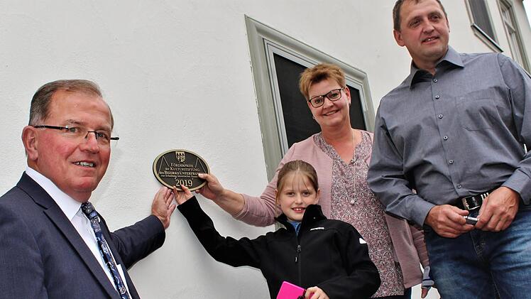 Hierhin könnte die Plakette passen. Bezirkstagspräsident Erwin Dotzel und Familie Sitzmann vor dem ausgezeichneten Haus im Hammelburger Stadtteil Pfaffenhausen.Werner Vogel