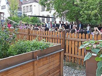 Schüler und Schülerinnen, die Lehrerschaft und die geladenen Gäste bestaunen den neu angelegten Schulgarten der Pestalozzi Grundschule.