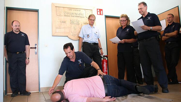 Kann der Feuerwehranwärter eine Person in die stabile Seitenlage versetzen? Die Ausbilder simulieren eine typische Prüfungssituation. Jürgen Schemmel (helles Hemd) von der Feuerwehrschule Würzburg informierte in der Kissinger Feuerwache über die neue "Modularisierte Truppausbildung". Foto: Ronald Heck