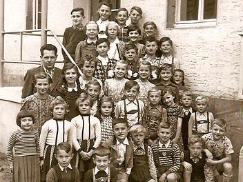 Diese Aufnahme zeigt den Schuljahrgang 1955/56. Unterrichtet wurden die Kinder von Lehrer Franz Buschbacher (3. Reihe, links). Sein gleichnamiger Sohn, der Co-Autor des Buches, ist in der 2. Reihe als Zweiter von rechts zu sehen, dessen Zwillingsschwestern stehen in der dritten Reihe und tragen gepunktete Kleider.