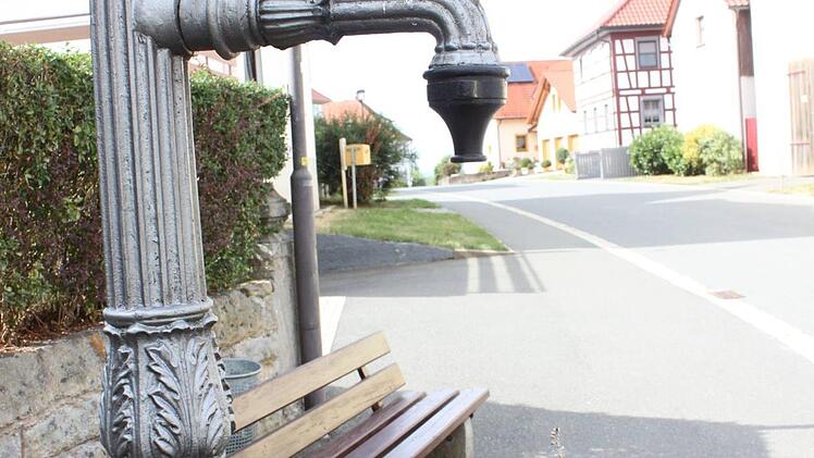 Blumengeschmückter Brunnen an der Straße vor dem Dorfplatz