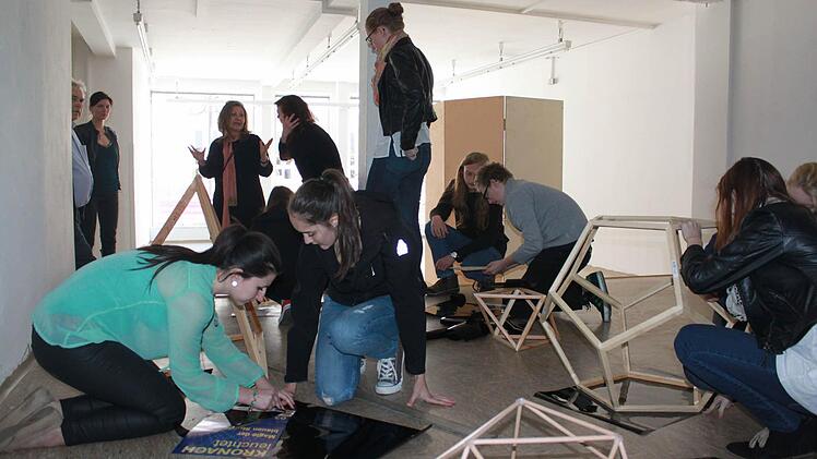 Schüler arbeiten an ihren Ausstellungsstücken und schneiden geometrische Formen aus, mit denen sie die Schaufenster bekleben. Mit im Bild sind (hinten von links) Hartmut Nenninger (Mitorganisator von "Kronach leuchtet") sowie die beiden Künstlerinnen Daniela Faber und Andrea Partheymüller-Gerber. Foto: Alexander Löffler