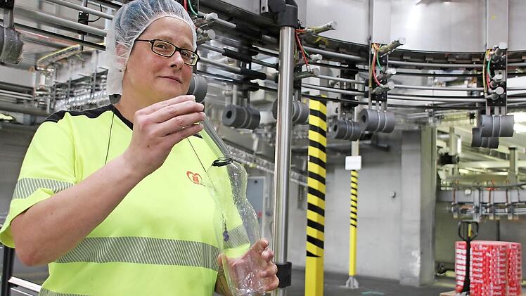 Schichtleiterin Tanja Schaupp zeigt einen Flaschenrohling sowie eine daraus gefertigte maschinengeblasene Plastikflasche.