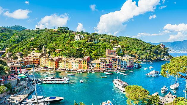 Schöne Aussicht auf Portofino, Ligurien, Italien Beautiful view of Portofino, Liguria, Italy Portofino ist ein Fischerdorf, das an der italienischen Riviera südöstlich von Genua liegt. Pastellfarbene Häuser, Luxusboutiquen und Fischrestaurants säumen die Piazzetta, einen kleinen, kopfsteingepflasterten Platz mit Blick auf den Hafen, wo Super-Yachten vor Anker liegen. Von der Piazzetta führt ein Weg zum Castello Brown, einer Festung aus dem 16. Jahrhundert. Das dazugehörige Museum bietet neben seinen Kunstausstellungen auch einen Panoramablick auf den Ort und das Ligurische Meer.