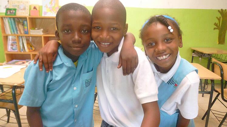 Die drei Kinder strahlen, stehen im Klassenzimmer. Foto: Maria Zink