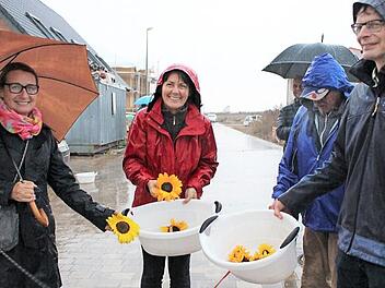 Pfarrerin Angelika Steinbauer (Mitte) und Pfarrer Andreas Steinbauer (rechts) hatten zur Begrüßung der Neubürger Sonnenblumen dabei. Die Neubürger Annette (links) und Jürgen Oeser (halb verdeckt) freuen sich - trotz Regen.  Foto: Evi Seeger