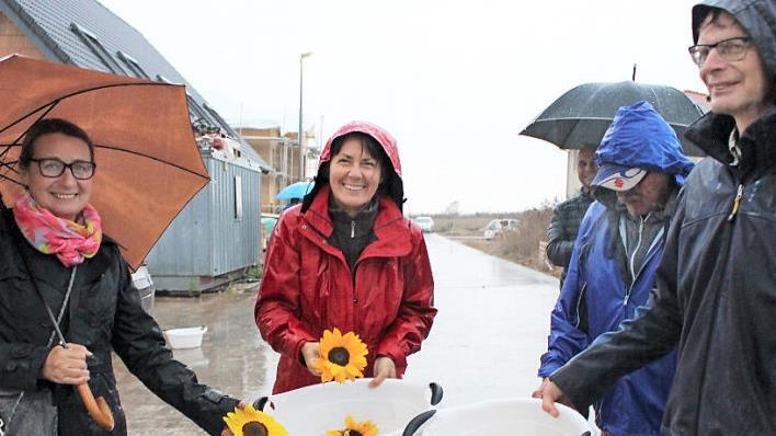 Pfarrerin Angelika Steinbauer (Mitte) und Pfarrer Andreas Steinbauer (rechts) hatten zur Begrüßung der Neubürger Sonnenblumen dabei. Die Neubürger Annette (links) und Jürgen Oeser (halb verdeckt) freuen sich - trotz Regen.  Foto: Evi Seeger