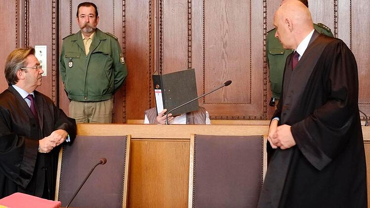 Der Angeklagte verbirgt sein Gesicht hinter einem Aktenordner. Foto: Nikolas Pelke